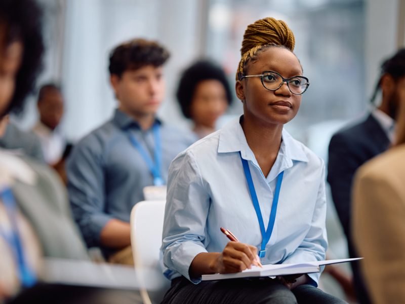 African American businesswoman taking notes while participating in an education event at convention center.