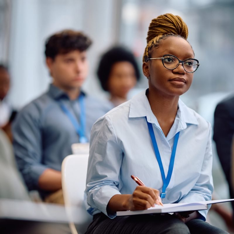 African American businesswoman taking notes while participating in an education event at convention center.